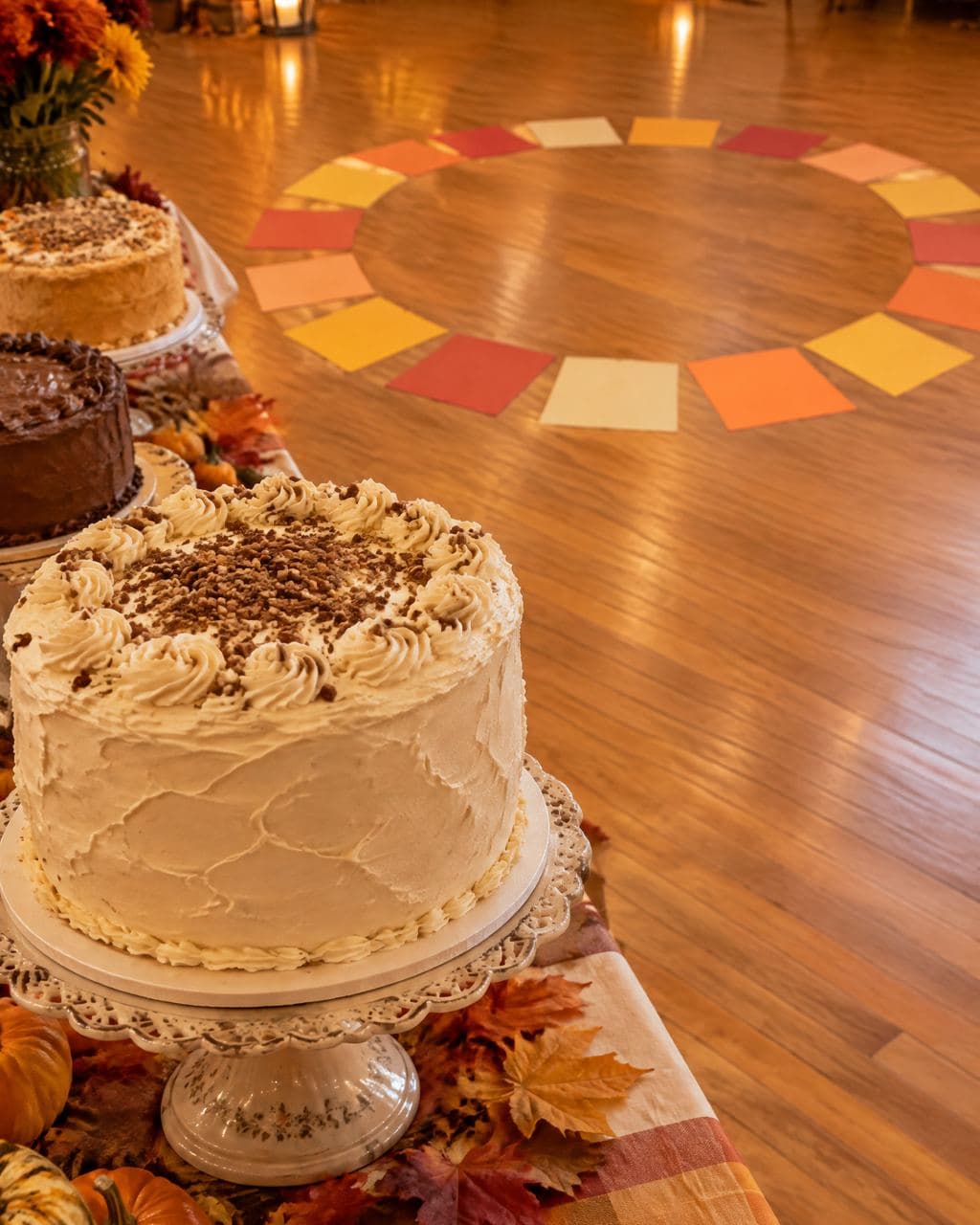 A frosted layer cake on a stand beside a circle of colored cake-walk squares on the floor