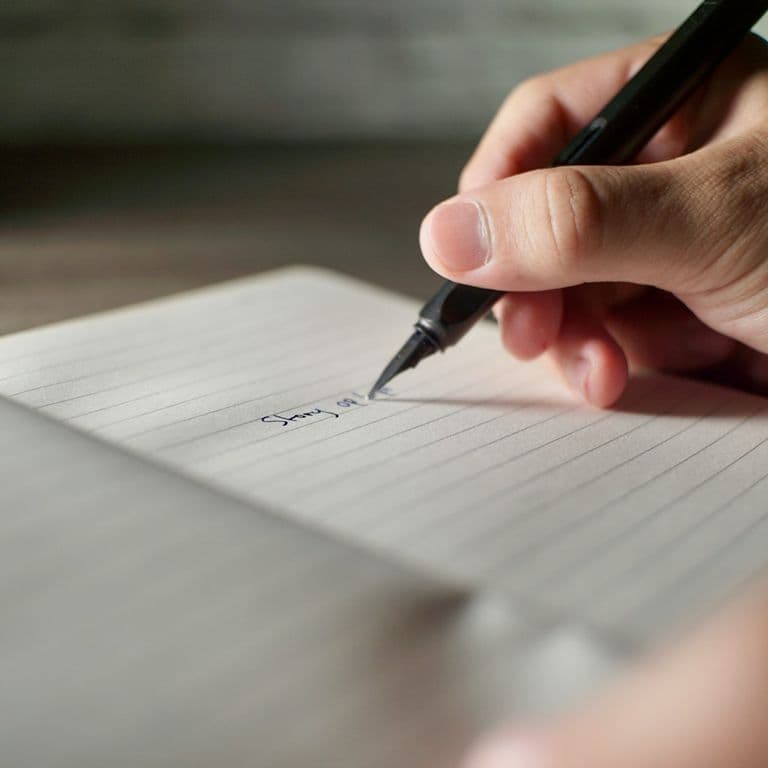 A student writing by hand in a lined notebook