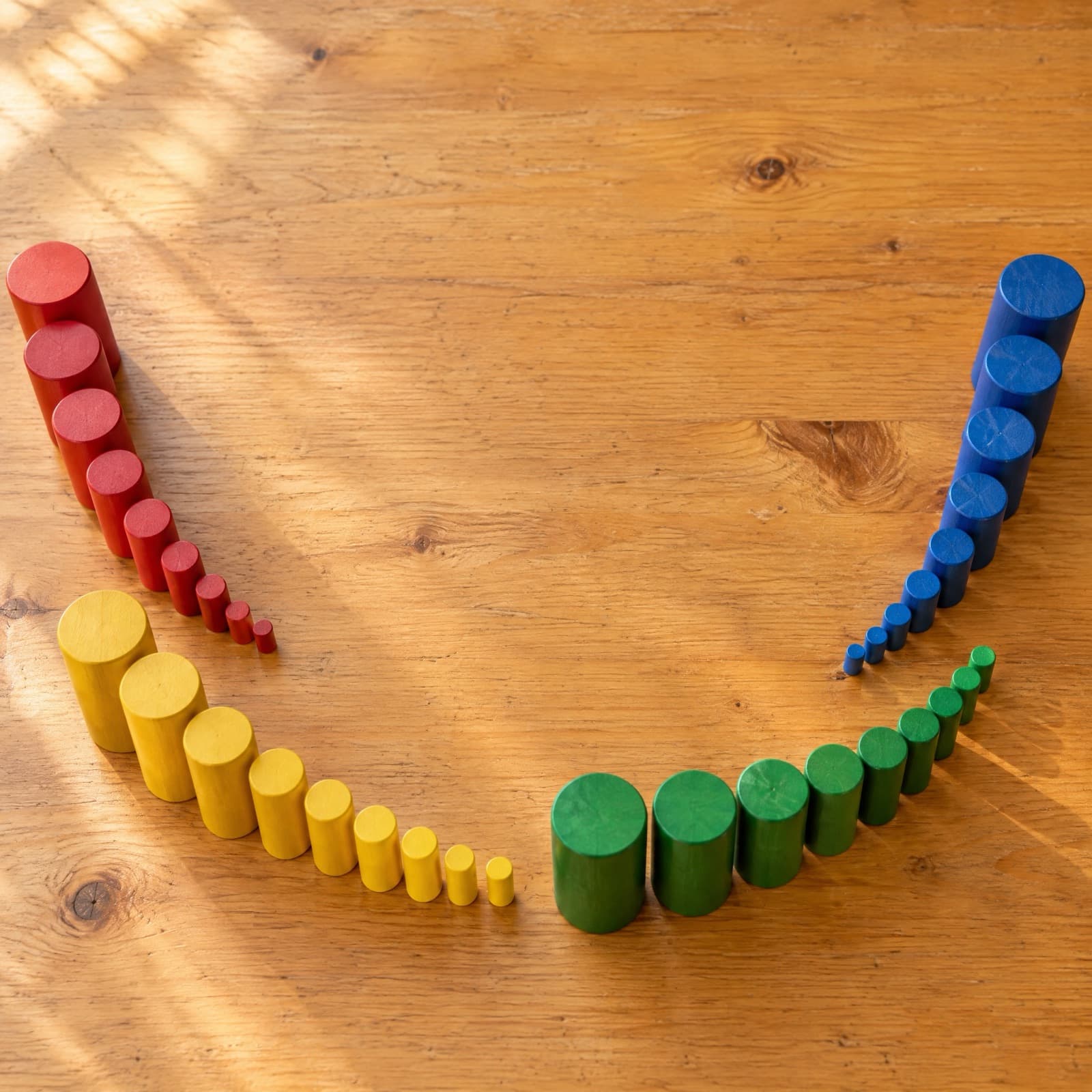 Rows of coloured wooden cylinders arranged from largest to smallest on a wooden floor