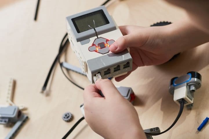 A student's hands wiring a cable into a programmable robotics controller
